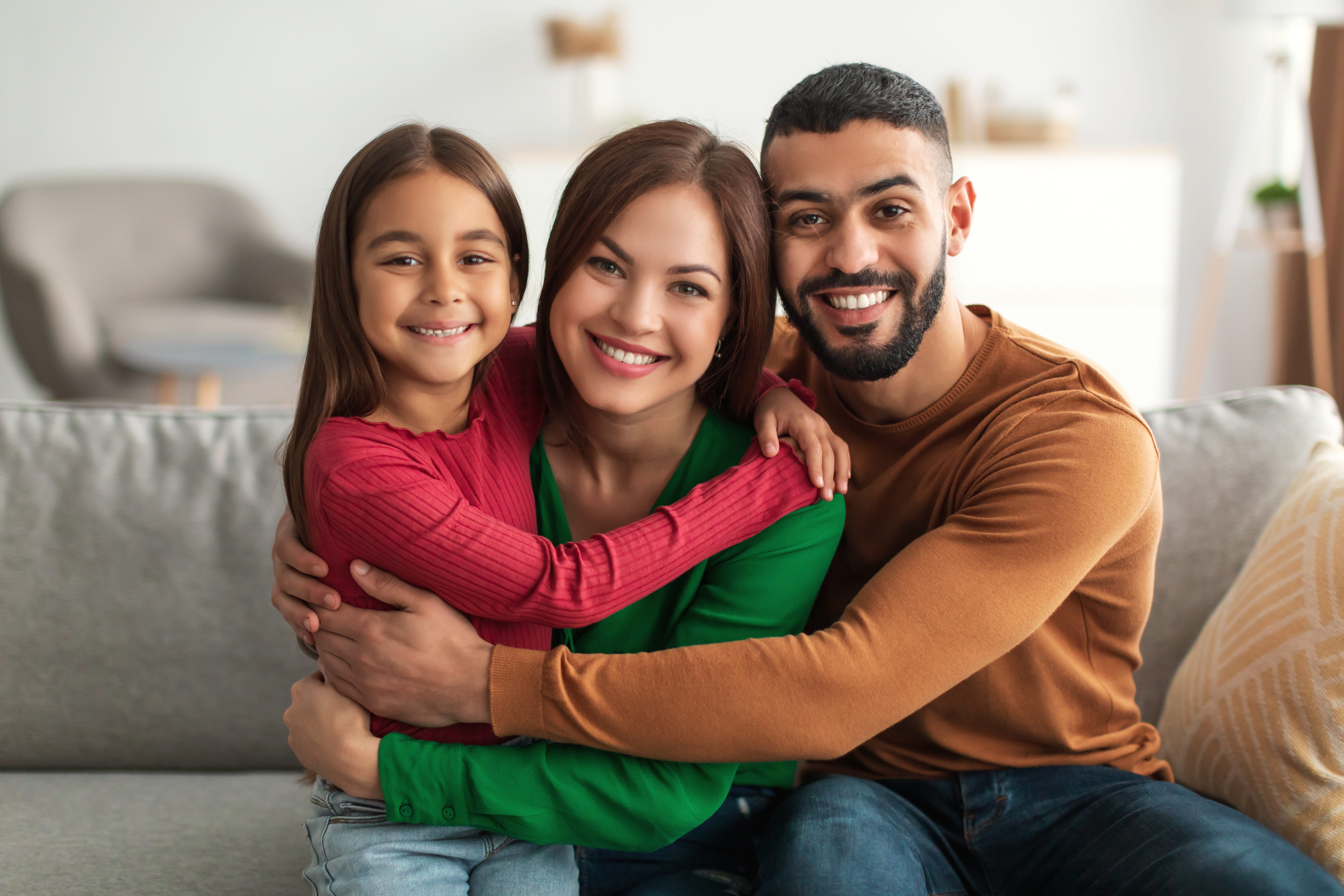 Lächelnde Familie mit Kind umarmt sich auf dem Sofa